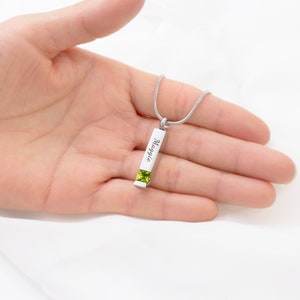 May include: Silver necklace with a rectangular pendant engraved with the name "Maggie" and a green gemstone.