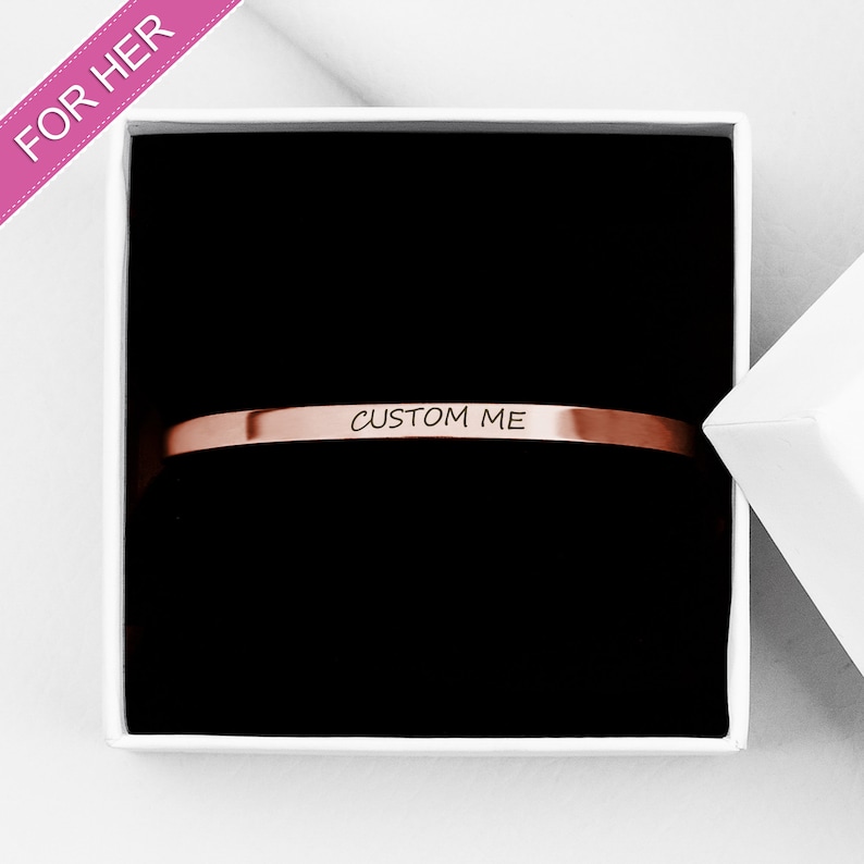 Op de afbeelding: Een ros&eacute;gouden armband in een witte doos met de woorden "CUSTOM ME" gegraveerd op de armband.