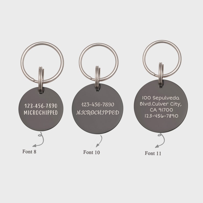 Op de afbeelding: Drie zilveren sleutelhangers met ronde zwarte labels. De labels hebben verschillende lettertypen en tekst. Het eerste label zegt "123-456-7890 MICROCHIPPED" in een klein lettertype. Het tweede label zegt "123-456-7890 MICROCHIPPED" in een iets groter lettertype. Het derde label zegt "100 Sepulveda Blvd.Culver City, CA 91700 123-456-7890" in een groter lettertype.