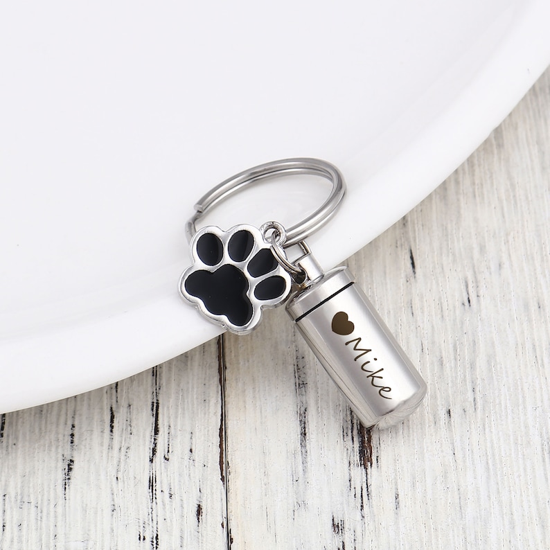 May include: Silver keychain with a black paw print charm and a small silver cylinder with the inscription "Mike" and a heart.