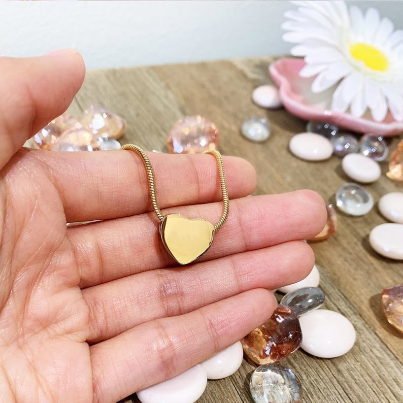 Puede incluir: Un collar de oro con un colgante en forma de coraz&oacute;n en una cadena delicada. El colgante es liso y brillante, y la cadena es fina y delicada.