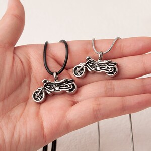 Puede incluir: Dos collares con colgante de motocicleta de plata, uno con un cord&oacute;n de cuero negro y el otro con una cadena de plata.