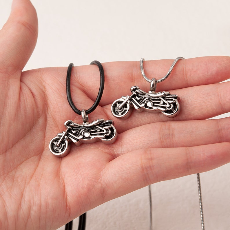 Puede incluir: Dos collares con colgante de motocicleta de plata, uno con un cord&oacute;n de cuero negro y el otro con una cadena de plata.