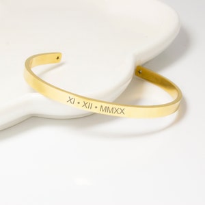 Op de afbeelding: Gouden armband met een gegraveerde inscriptie die "XI.XII.MMXX" luidt.