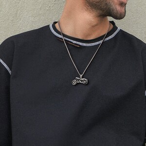 Puede incluir: Un collar con un colgante de plata en forma de motocicleta en un cord&oacute;n de cuero marr&oacute;n. El colgante es una representaci&oacute;n realista y detallada de una motocicleta.