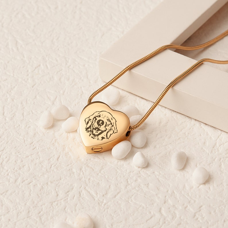 May include: Gold heart-shaped cremation necklace with a chain and a photo of a dog engraved on the front.