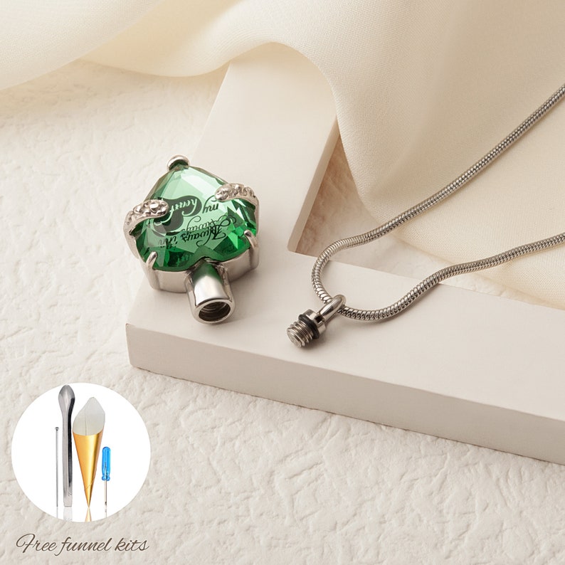 May include: A green crystal heart-shaped cremation necklace with a silver chain. The pendant has an inscription that reads "I carry you with me always". The necklace comes with a free funnel kit.