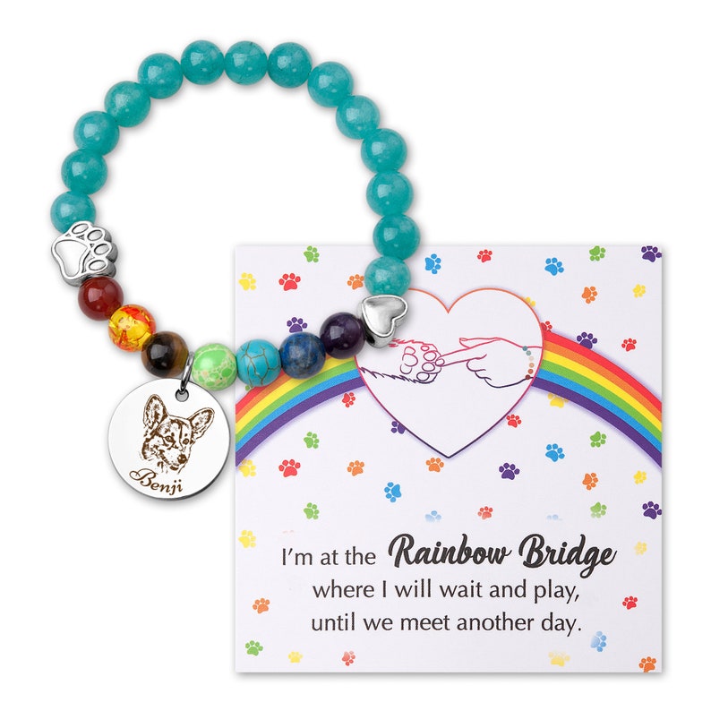 May include: A turquoise beaded bracelet with a charm featuring a paw print and a dog's face. The charm also has the name "Benji" engraved on it. The bracelet comes with a card that reads "I'm at the Rainbow Bridge where I will wait and play, until we meet another day."