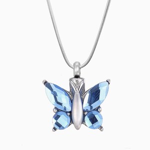 May include: A silver chain necklace with a blue crystal butterfly pendant. The butterfly has a detailed design and is a popular choice for memorial jewelry.