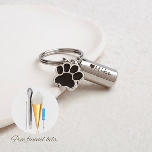 May include: Silver keychain with a small cylinder charm engraved with "Mike" and a black paw print charm. The keychain comes with a small funnel kit for filling the cylinder charm.