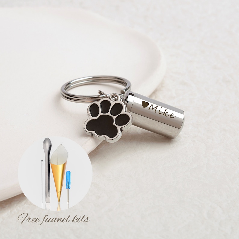 May include: Silver keychain with a small cylinder charm engraved with "Mike" and a black paw print charm. The keychain comes with a small funnel kit for filling the cylinder charm.