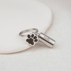 May include: Silver keychain with a paw print charm and a small cylinder engraved with the name "Stella" and a heart.