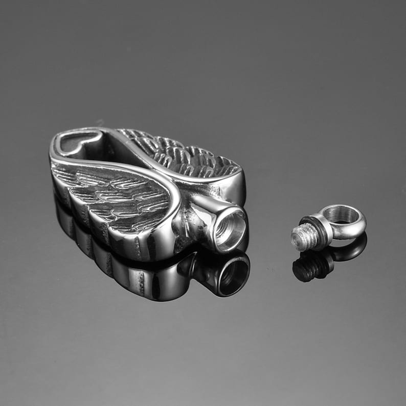 Puede incluir: P&eacute;ndulo de cremaci&oacute;n de metal plateado en forma de alas de &aacute;ngel. El p&eacute;ndulo est&aacute; abierto por un lado y tiene un tap&oacute;n de rosca en el otro lado. El p&eacute;ndulo se muestra junto a su tap&oacute;n de rosca separado.