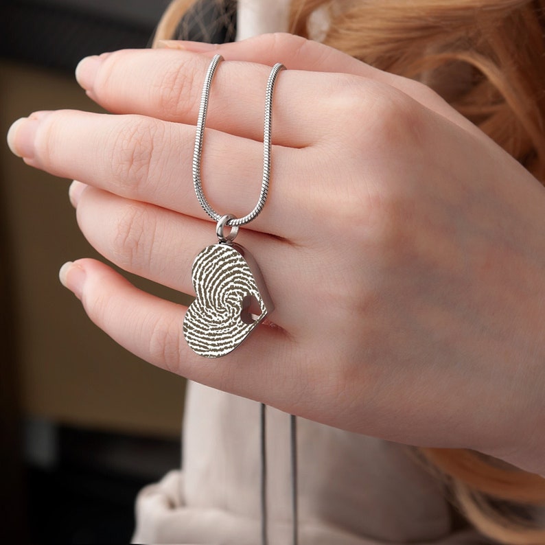 Puede incluir: Un collar de plata con un colgante en forma de coraz&oacute;n con un dise&ntilde;o de huella digital. El colgante tiene una peque&ntilde;a abertura en la parte superior.