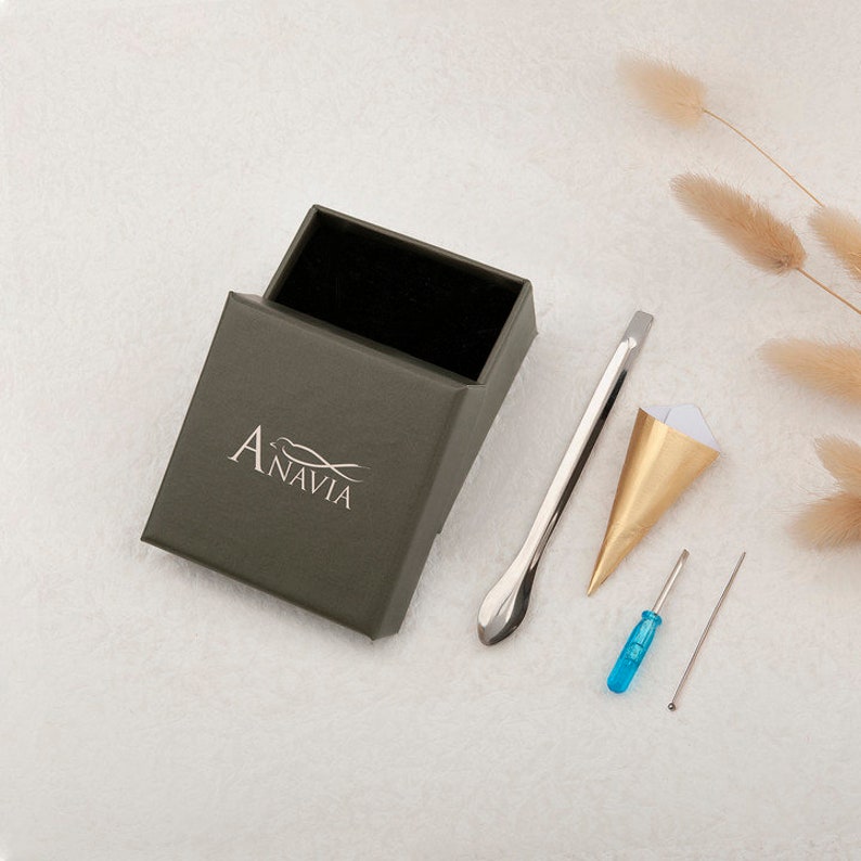 May include: A green box with the word "Anavia" printed on it, a silver tool with a rounded end, a gold paper cone, a blue screwdriver, and a silver needle.