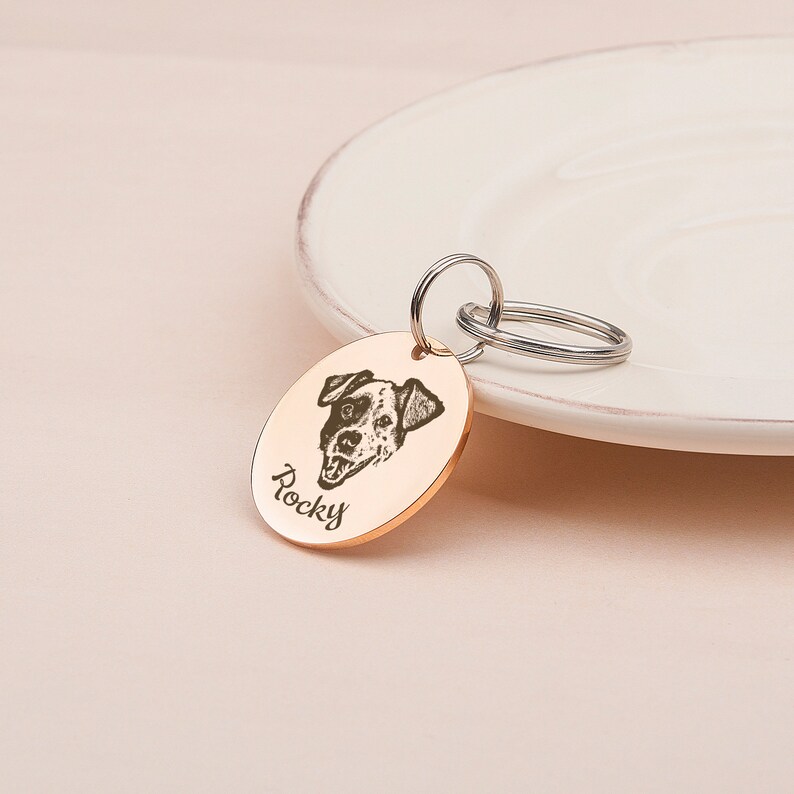 May include: A round, gold-colored dog tag with a black and white photo of a dog and the name "Rocky" engraved on it.