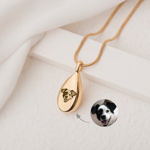 May include: Gold teardrop-shaped pendant necklace with a small engraved image of a dog's face. The pendant is on a gold chain.