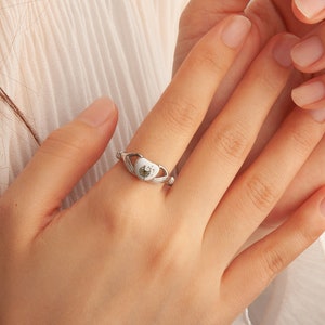 May include: A silver ring with a white heart-shaped setting featuring a dandelion design.