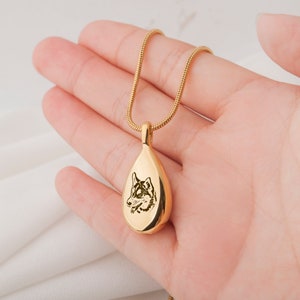 May include: Gold teardrop-shaped pendant necklace with a dog's face engraved on the front.