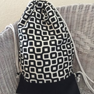 Könnte beinhalten: Schwarze und weiße geometrische gemusterte Kordeltasche mit schwarzem Boden. Die Tasche ist aus Stoff und hat einen weißen Kordelzug.