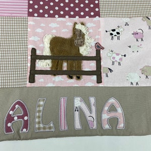 Op de afbeelding: Een roze en bruine patchwork babydeken met een bruine paardenapplicatie en de naam "ALINA" geborduurd in bruine letters.
