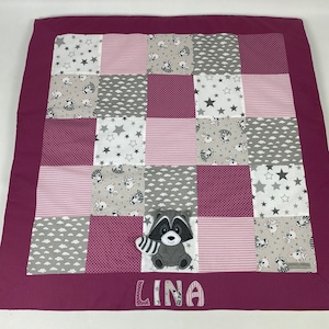 Può includere: Una copertina per neonati in patchwork rosa e grigio con un'applicazione di procione e il nome "LINA" ricamato in basso.