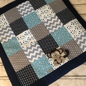 Könnte beinhalten: Eine blaue und graue Patchwork-Babydecke mit einem braunen Affen-Applikationen. Die Decke hat einen dunkelblauen Rand.