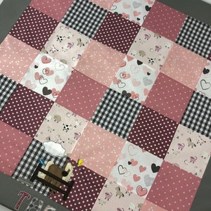 Op de afbeelding: Een roze en bordeauxrode patchwork babydeken met een grijze rand. De deken heeft verschillende patronen, waaronder harten, stippen en boerderijdieren. De naam "THEA" is op de onderkant van de deken geborduurd.