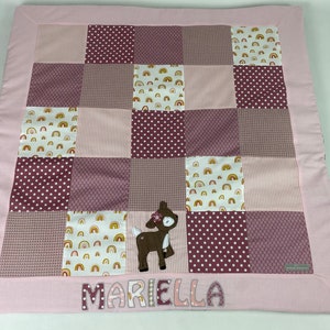 Può includere: Una copertina per neonati in patchwork rosa e marrone con un'applicazione a forma di cervo e il nome "Mariella" ricamato in basso.