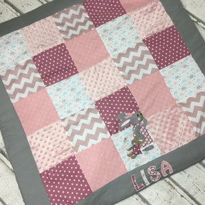 May include: A pink and grey patchwork baby blanket with a bunny and the name "LISA" embroidered on it.