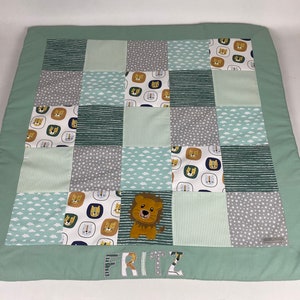 Op de afbeelding: Een groene en witte patchwork speelmat met een leeuwenontwerp en de naam "FRITZ" geborduurd aan de onderkant.