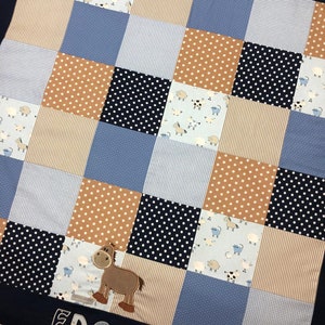 Könnte beinhalten: Eine blaue und braune Patchwork-Babydecke mit einer Pferdeapplikation und dem Namen "EDGAR", der auf dem unteren Rand gestickt ist.