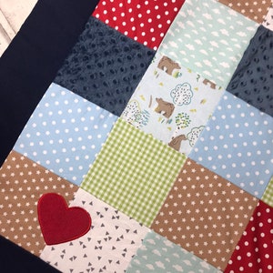 Peut inclure: Une courtepointe en patchwork avec une variété de motifs et de couleurs, notamment le rouge, le bleu, le vert, le marron et le blanc. La courtepointe présente un cœur rouge au centre.
