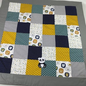 Peut inclure: Un tapis de jeu en patchwork avec une variété de motifs et de couleurs, notamment le jaune, le bleu, le blanc et le vert. Le tapis de jeu présente une applique en forme de panda au centre.