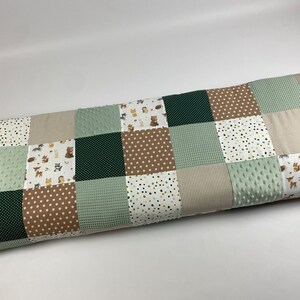 Könnte beinhalten: Eine Patchwork-Decke mit verschiedenen grünen, braunen und weißen Stoffen. Die Decke besteht aus Quadraten mit unterschiedlichen Mustern, darunter Punkte, Sterne und Tiermotive.
