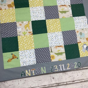 Könnte beinhalten: Eine graue und weiße Patchwork-Babydecke mit einem grünen, gelben und braunen Tierdruck. Die Decke hat einen grauen Rand mit dem Namen "ANTON 23.11.2020" bestickt.