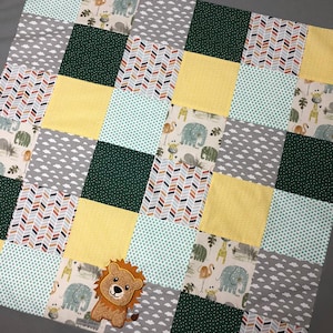 Könnte beinhalten: Eine Patchwork-Babydecke in Grün, Gelb und Grau. Die Decke hat verschiedene Muster, darunter Chevron, Punkte und Wolken. Die Decke ist mit dem Namen "LEON" in gelben Buchstaben personalisiert.