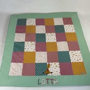 Könnte beinhalten: Eine grüne Patchwork-Spielmatte mit Giraffen- und Regenbogen-Design. Die Spielmatte hat einen grünen Rand und der Name "LOTTA" ist unten aufgenäht.