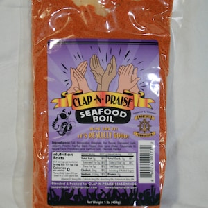 Könnte beinhalten: Ein roter und weißer Beutel mit Clap-N-Praise Seafood Boil Gewürz. Der Beutel zeigt einen Cartoon-Krabben und den Text "Just try it! It's really good!" Der Beutel wiegt 1 Pfund (454 Gramm).