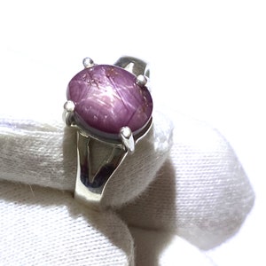 Puede incluir: Un anillo de plata con una piedra preciosa ovalada de color rosa. La piedra preciosa tiene un patrón en forma de estrella.