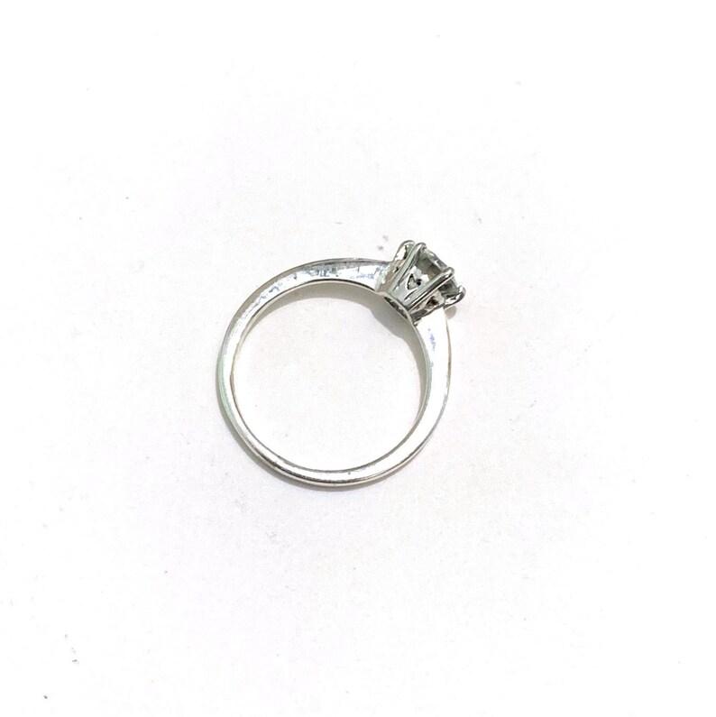 Op de afbeelding: Een zilveren ring met een enkele ronde diamant in een kraalbezetting.