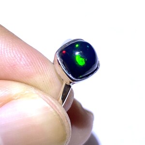 Könnte beinhalten: Ein Silberring mit einem schwarzen Opal-Edelstein. Der Opal zeigt grüne und rote Farbschimmer.