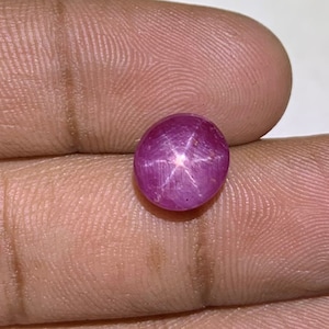 Könnte beinhalten: Ein runder, rosafarbener Sternrubin-Edelstein mit einem sechszackigen Stern in der Mitte.