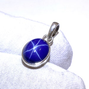Może przedstawiać: Srebrny wisiorek z niebieskim szafirem gwiaździstym z wzorem gwiazdy.