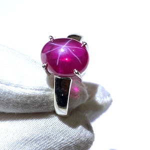 Peut inclure: Une bague en argent ornée d'une grosse pierre précieuse ronde, rouge foncé, avec un motif en étoile à six rayons. La pierre est sertie dans un sertissage classique à quatre griffes, mettant en valeur sa couleur vibrante et son effet optique unique. Le jonc de la bague est en argent poli.