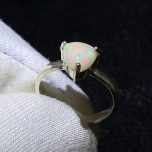 Könnte beinhalten: Ein Silberring mit einem birnenförmigen Opal-Edelstein. Der Opal zeigt ein Farbspiel mit roten, grünen und orangen Blitzen. Der Ring hat ein schlichtes, poliertes Silberdesign, das den Edelstein hervorhebt.