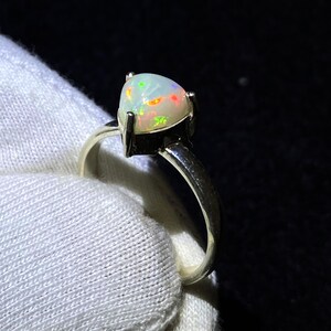 Könnte beinhalten: Ein Silberring mit einem dreieckigen Opal-Edelstein. Der Opal ist weiß mit grün, rot und orangefarbenen Blitzen.