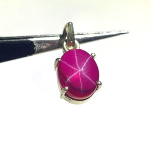 May include: A silver pendant featuring a pink star ruby gemstone with a six-pointed star.