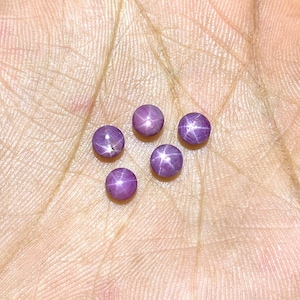 Könnte beinhalten: Fünf violette Stern-Saphire mit einem sternförmigen Muster in der Mitte jedes Steins.