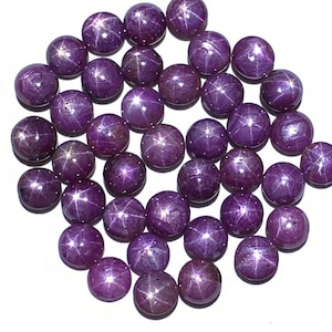 Könnte beinhalten: Eine Sammlung von 30 runden, violetten Sternrubin-Cabochons. Die Cabochons sind glatt und poliert mit einem sternförmigen Muster, das auf jedem sichtbar ist.